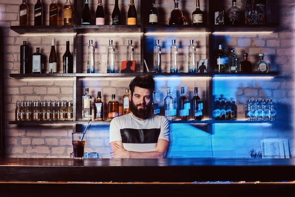 Fiducioso barbuto barista posa con le braccia incrociate dietro bancone del bar in discoteca . — Foto Stock
