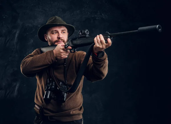 Hunter sostiene un rifle y apunta a su objetivo o presa. Estudio foto contra fondo oscuro de la pared —  Fotos de Stock