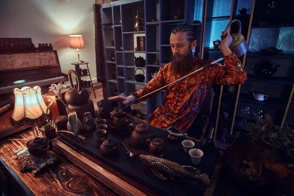 Китайська чайна церемонія. Кавказький майстер в кімоно робить натуральний чай в темній кімнаті з дерев'яним інтер'єром, використовуючи чайник з довгим носиком. Традиції, здоров'я, гармонія. Китайська чайна церемонія — стокове фото