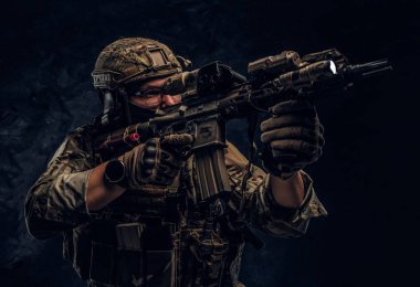 Close-up studio photo against a dark wall. The elite unit, special forces soldier in camouflage uniform holding an assault rifle with a laser sight and aims at the targe clipart