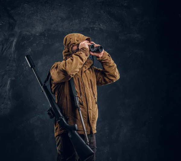 Κυνηγός με καραμπίνα να βλέπει μέσα από κιάλια. Φωτογραφία στούντιο ενάντια σκούρο τοίχο φόντο — Φωτογραφία Αρχείου