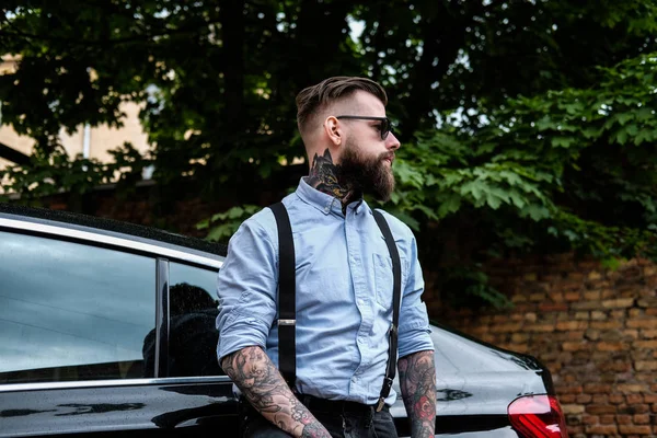 Atractivo hombre barbudo se apoya en su coche . — Foto de Stock