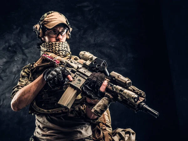 Plně vybavené voják v maskování jednotné drží útočná puška. Studiové fotografie tmavé stěny — Stock fotografie
