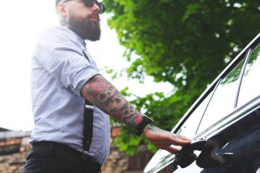 Tattoed sakallı adam arabasını açıyor. 