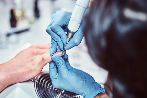 Beautician master in gloves applying nail drill to trim and remove cuticles. Hardware manicure in a beauty salon