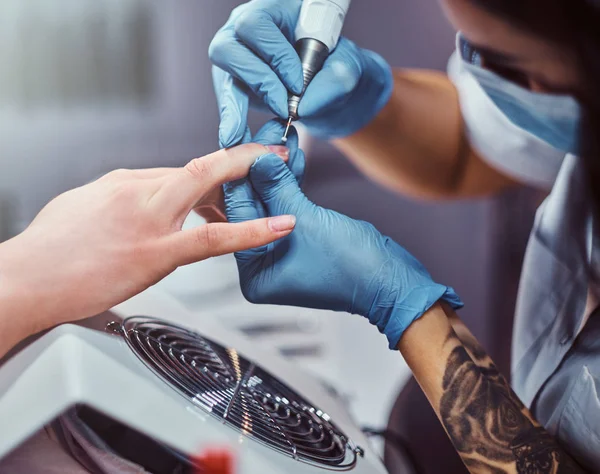 Beautician master in gloves applying nail drill to trim and remove cuticles. Hardware manicure in a beauty salon