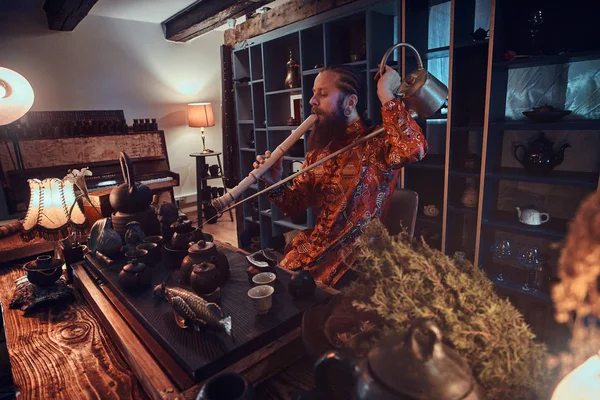 Tea master in kimono making natural tea and playing on a bamboo flute, performs in the dark room with a wooden interior. — Stock Photo, Image