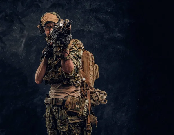 L'unità d'élite, soldato delle forze speciali in uniforme mimetica con un fucile d'assalto con mirino laser e mira al bersaglio. Studio foto contro un muro scuro — Foto Stock