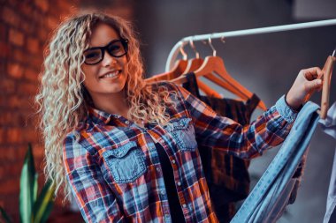 Gözlük ve damalı gömlek gülümseyen mutlu kadın onu tatil için giysi seçer.