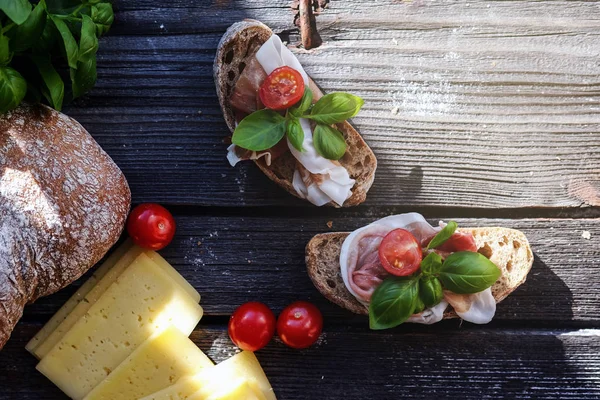 Kleine broodjes met vlees, cherry tomaten, kaas, brood en basilicum op de zwarte tafel. — Stockfoto