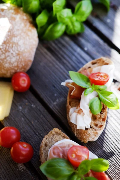 Kleine broodjes met vlees, cherry tomaten, kaas, brood en basilicum op de zwarte tafel. — Stockfoto