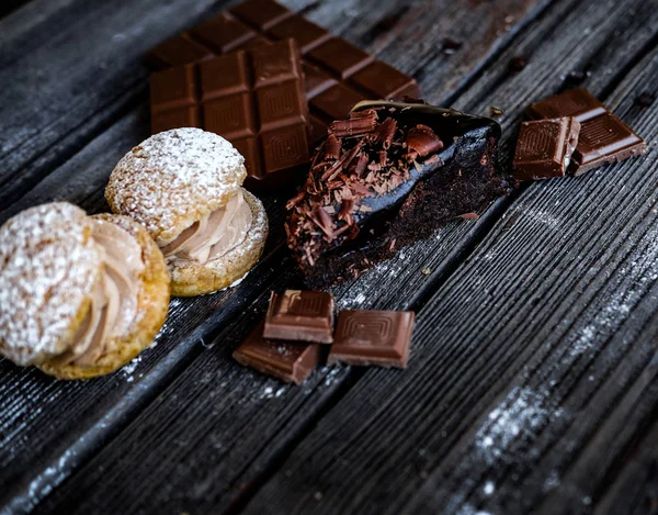 Rebanada de brownie, dos pasteles de sándwich y paces de chocolate en la mesa negra . — Foto de Stock