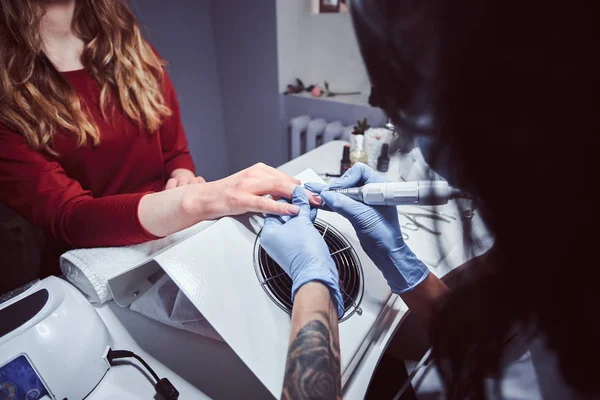 Beautician master in gloves applying nail drill to trim and remove cuticles. Hardware manicure in a beauty salon