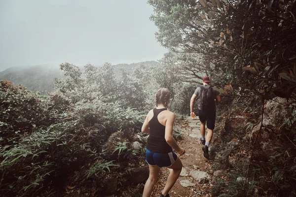 Jeune couple est en cours d'exécution par le chemin dans les montagnes forestières — Photo