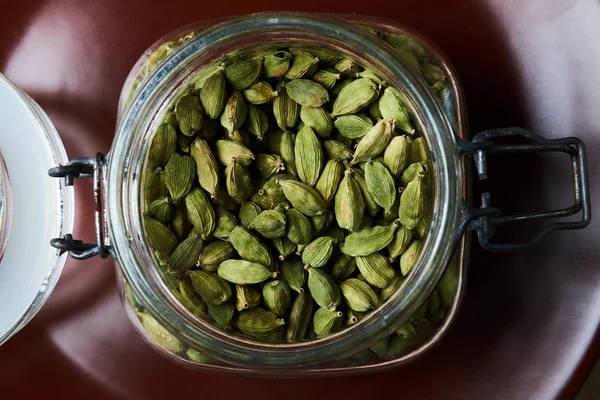 Closeup proto of glass jar full of green cardamom pods on brown plate — Stock Photo, Image