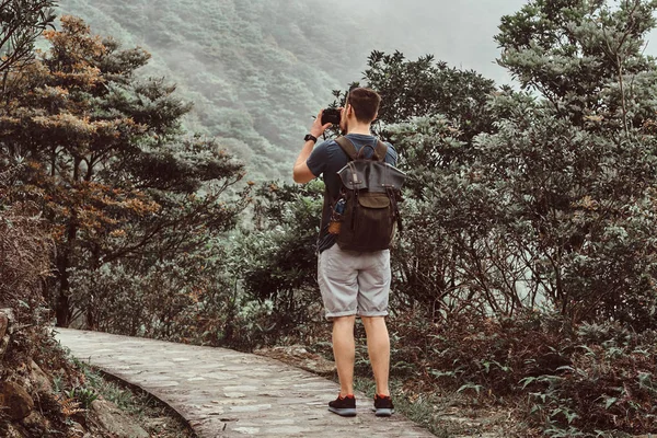 Joven con la mochila está tomando fotos de la hermosa naturaleza en su cámara de fotos —  Fotos de Stock