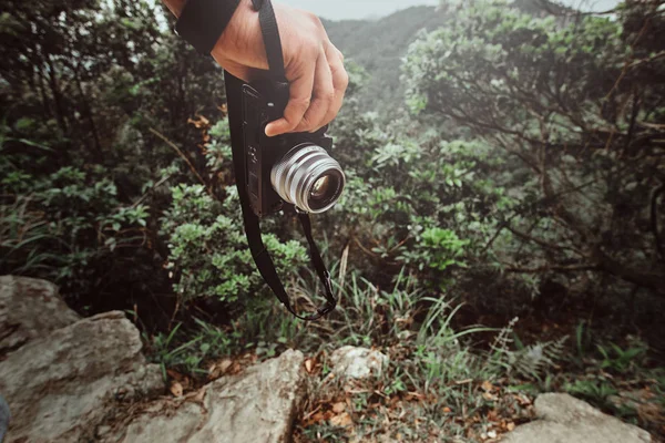 Man houdt camera in zijn hand terwijl wandelen door het pad gooi de groene bergen — Stockfoto