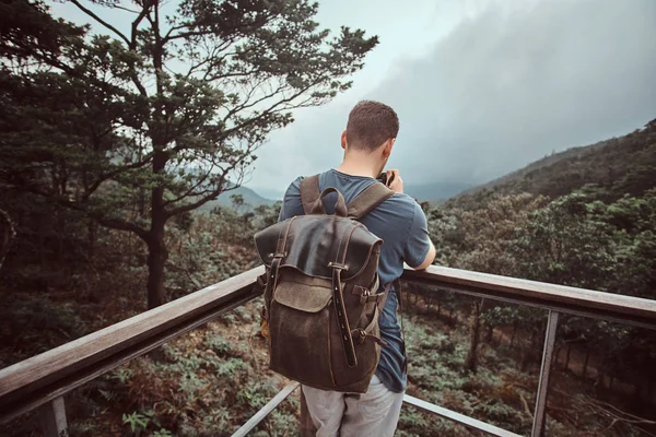 Hombre joven con mochila está tomando una foto de la hermosa naturaleza mientras está de pie en el balcón turístico — Foto de Stock