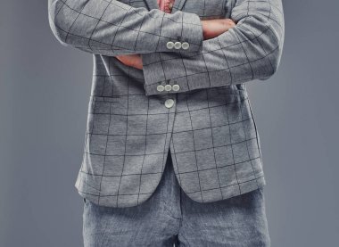 Gri damalı blazer ve gri arka planda gri pantolon çapraz elleri ile Adam