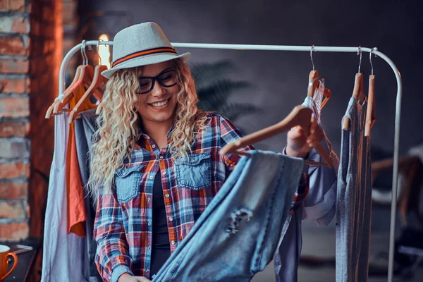 Pretty happy woman in glasses, hat and checkered shirt chooses jeans for her holidays — Stock Photo, Image