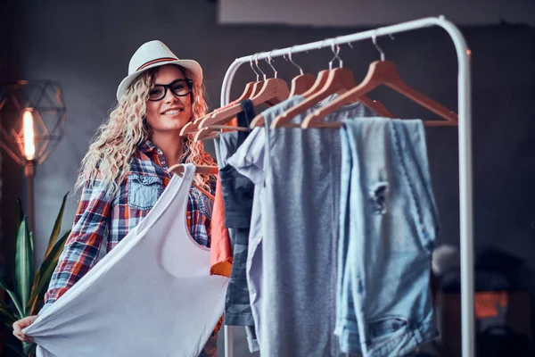 Wanita muda yang bahagia dengan topi dan kacamata yang rapi di lemari pakaiannya untuk musim panas di loteng modern . — Stok Foto