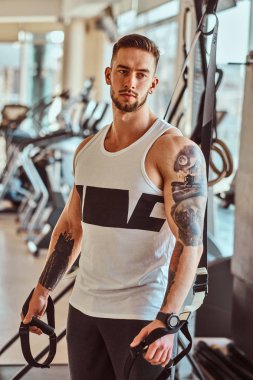 Güçlü kaslı adam güneşli spor salonunda eğitim cihazları yanında poz