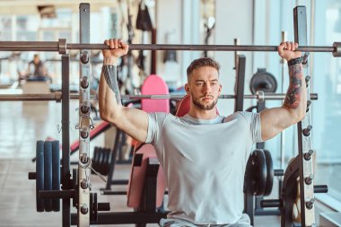 Genç dövmeli vücut geliştirici spor salonunda halterle antrenman yapıyor.