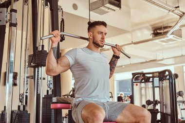 Genç dövmeli adam spor salonundaki eğitim aletleri için egzersiz yapıyor.