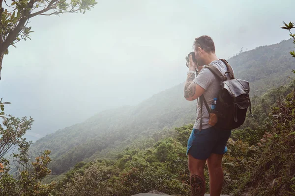 Sırt çantalı genç adam fotoğraf makinesiyle doğanın güzel fotoğraflarını çekiyor. — Stok fotoğraf