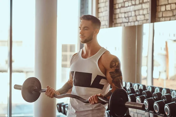 Atractivo culturista tatuado está haciendo sus ejercicios con barra de pesas en el gimnasio — Foto de Stock