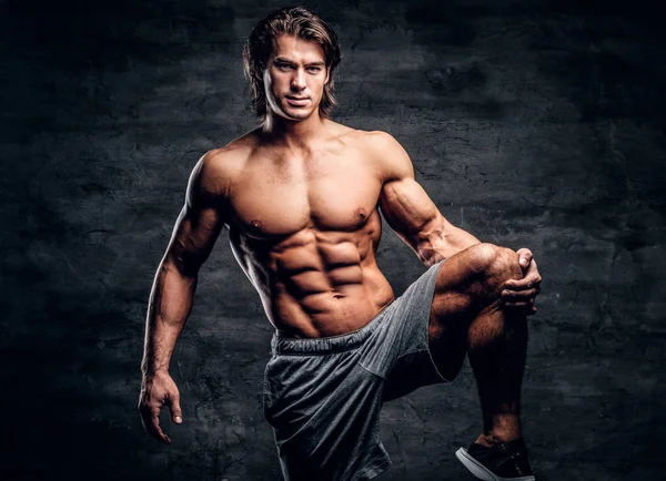 Glimlachend aantrekkelijk bodybuilder met naakte torso doet been strechening — Stockfoto