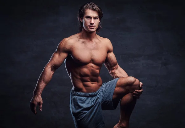 Smiling attractive bodybuilder with naked torso is doing leg strechening — Stock Photo, Image