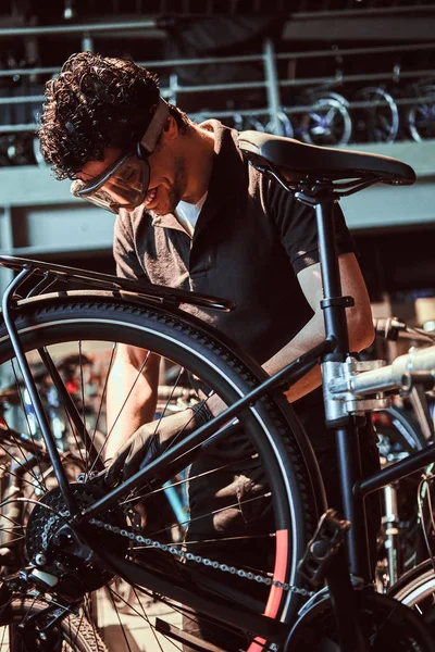 Pensativo maestro diligente en gafas protectoras es la fijación de la bicicleta en el taller — Foto de Stock