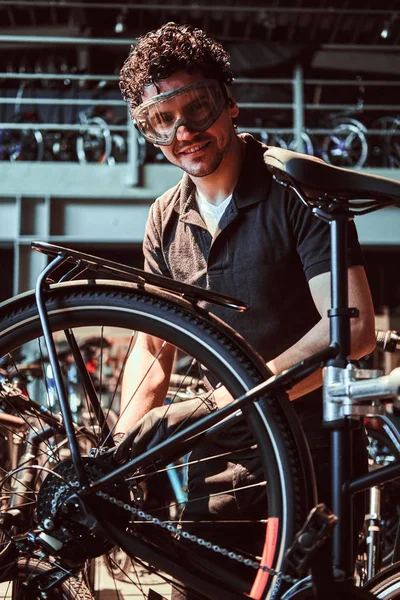 Pensativo maestro diligente en gafas protectoras es la fijación de la bicicleta en el taller — Foto de Stock
