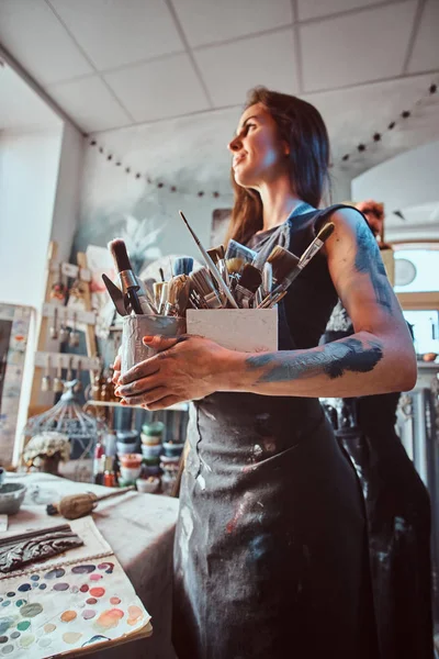 Young attractive painter is posing with brushes in her own cozy workshop — 스톡 사진