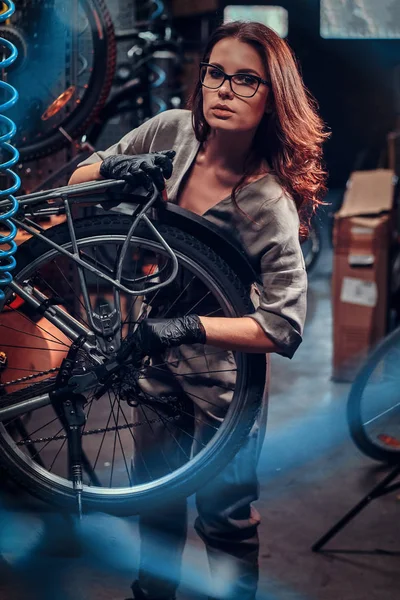 Diligent beautiful girl is repairing bicycle at busy workshop