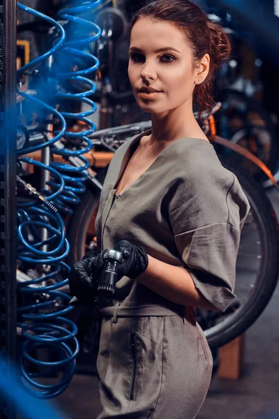 Diligent beautiful girl is repairing bicycle at busy workshop between pneumatic wires