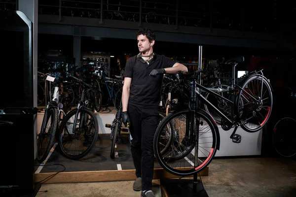 Joven maestro pensativo es escalofriante al lado de la bicicleta después de un largo día duro en su taller — Foto de Stock