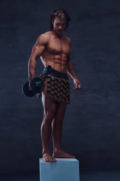 Beautiful shirtless bodybuilder is posing with dumbbell on pedestal — Stock Photo, Image