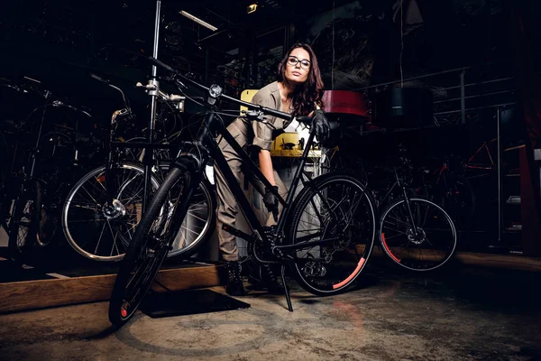 Mujer atractiva está arreglando la bicicleta en el taller ocupado . —  Fotos de Stock