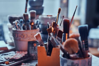 Kavanozlarda sanatçı masasında bir sürü farklı fırça. Masada artistikler var.
