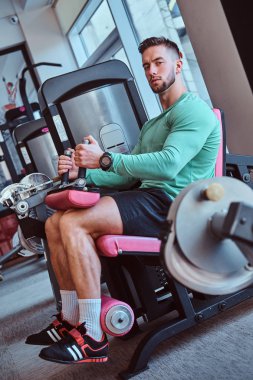 Güçlü dalgın adam spor salonunda eğitim aparatları üzerinde oturuyor ve bacak egzersizleri yapıyor