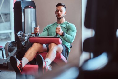 Güçlü dalgın adam spor salonunda eğitim aparatları üzerinde oturuyor ve bacak egzersizleri yapıyor