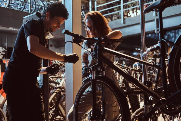 Молодой мастер и его привлекательный ученик чинят клиентам велосипеды в мастерской — стоковое фото