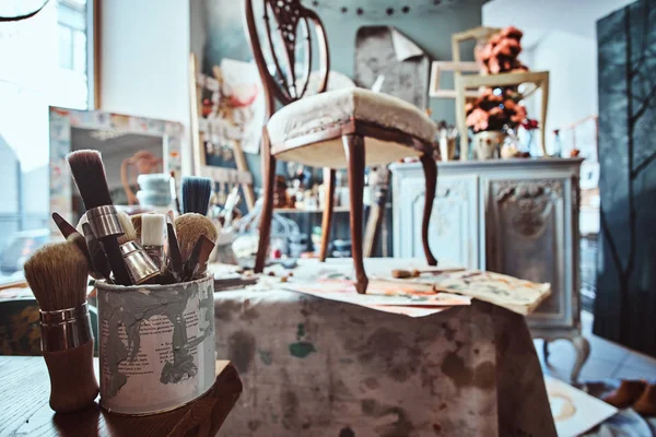 Künstlerwerkstatt mit notwendiger Ausrüstung wie Farbe, Pinsel, Rahmen, Blumen, Tisch, Stuhl und Schrank. — Stockfoto