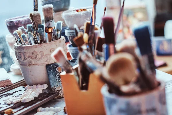 Muitos pincéis diferentes na mesa de artistas em jarros. Há artisticks bagunça na mesa — Fotografia de Stock