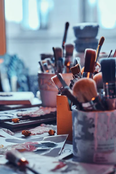 Muitos pincéis diferentes na mesa de artistas em jarros. Há artisticks bagunça na mesa — Fotografia de Stock