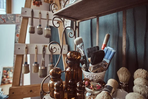 Frascos de vidrio, diferentes cepillos y otras herramientas en un estante en el estudio de arte — Foto de Stock
