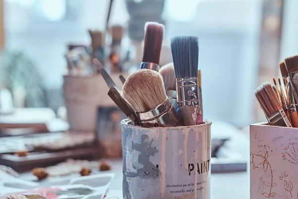 Muitos pincéis diferentes na mesa de artistas em jarros. Há artisticks bagunça na mesa — Fotografia de Stock