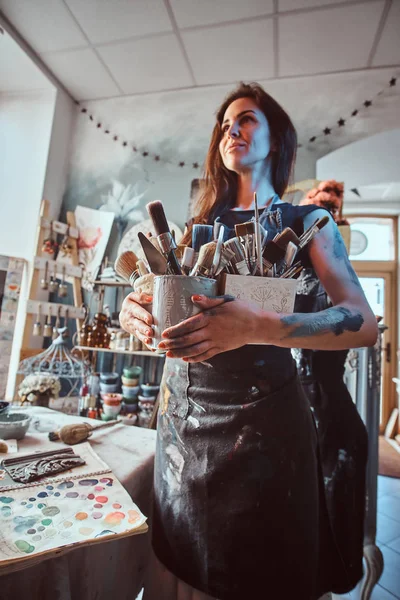 Молодая привлекательная художница позирует кистями в своей уютной мастерской — стоковое фото